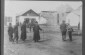 An elderly man in traditional dress with a cane poses among passersby in the marketplace near a store. 1920s © From the Archives of the YIVO Institute for Jewish Research